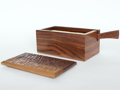 This Japanese-inspired walnut buttter-box has been crafted entirely with hand-tools and natural materials, all entirely food-safe.  The delicately bevelled edges and carved top are a pleasure to handle.  A butter knife, carved from the same piece of wood sits neatly inside ready for use.  H84 x D98 x W170mm  Irish craft handmade in Dublin, Ireland for Gallery33